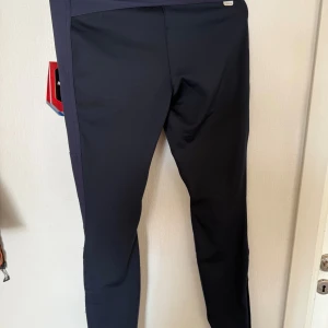 Svarta softshellbyxor från Icepark - Svarta softshellbyxor från Icepark med smal passform och dragkedjefickor framtill. Byxorna har bälteshällor, knapp och dragkedja i midjan samt förstärkta partier vid knäna. Perfekta för utomhusaktiviteter och träning.