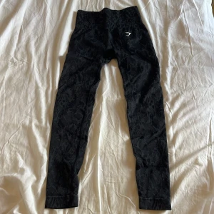Svarta leopardmönstrade leggings Gymshark - Snygga svarta leggings från Gymshark med diskret leopardmönster. Hög midja och tight passform som sitter på plats under träning, med en scrunch där bak. Stretchigt material som andas och ger bra rörelsefrihet. Perfekta för gymmet eller andra träningspass🖤