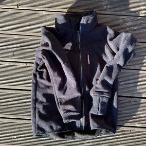 Svart fleecejacka Polarn O. Pyret 122 - Mörkblå fleecejacka från Polarn O. Pyret med hög krage och hel dragkedja framtill. Jackan har en bröstficka med dragkedja och ribbade muddar vid ärmsluten. Perfekt för kyliga dagar och enkel att slänga på sig.  Typ oanvänd nypris: 699kr                       Mitt pris: 349