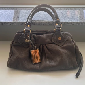 Brun handväska från Marc by Marc Jacobs - jättefin mörkbeige/grå väska i bra skick från Marc by Marc Jacobs i äkta läder och gulddetaljer. Långa bandet ingår.   Väskan är köpt från vinted ett par dagar sen men har tyvärr ångrat mig då jag behöver pengarna för annat.  storleken är i den lilla modellen och passar perfekt till allt. Mått: 34x18x12 cm (undersidan)  Skickar snabbt på posten och kan också tänka mig mötas upp i gbg!   Har du några mer frågor är det bara att ställa dom privat 🤍