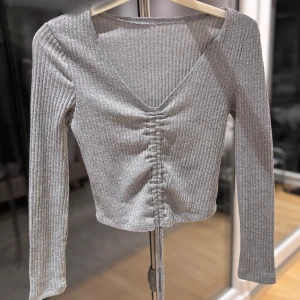 Grå topp - Snygg grå ribbad topp med lång ärm och croppad passform. V-ringning och trendig snörning framtill.