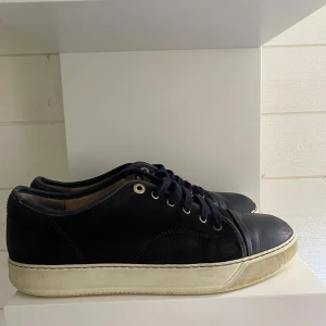 Mörkblåa lanvin skor  - Ett par slitna lanvin dbb1 skor mörkblå model finns skavanker såsom sulan är lite lös som visas och fram på cap toen är färgen borta och i kanterna på skorna är gummit borta samt sulerna är sönder och små hål. Innuti skorna  Storlek 43  