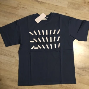 Blå Maison Margiela t-shirt - Helt ny blå t-shirt från Maison Margiela med ikoniskt grafiskt print framtill och klassisk rund hals. True to size passform och tillverkad i mjuk bomull. Perfekt för dig som gillar streetstyle och vill sticka ut med en unik design.