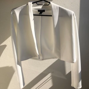 Vit  kavaj kortare modell - Elegant vit  kavaj med en kortare modell och öppen front. Aldrig använd endast testad. 