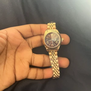 Guldig klocka från Nibosi med länkarmband - Snygg klocka från Nibosi i guldigt metallutförande med klassiskt länkarmband. Urtavlan är mörk med romerska siffror och datumvisning. Klockan levereras i originalask och har en elegant, tidlös design som passar till många stilar. Helt ny och aldrig använt om ni undrar om nåt skriv. Pris kan diskuteras 