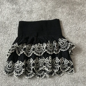 Svart volangkjol med broderi Lindex - Supersöt svart kortkjol från Lindex i storlek 146/152 men passar mig perfekt som har storlek xs, den harbred smock i midjan och flera lager volanger. Kjolen har vita broderade detaljer längs kanterna som ger en unik och lekfull look. Perfekt för dig som gillar att sticka ut med coola detaljer. 
