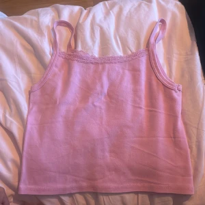 Rosa linnetopp från Brandy Melville - Supersöt ljusrosa linnetopp från Brandy Melville i 100% bomull. Toppen har smala axelband och en fin spetskant upptill som ger en gullig touch. Perfekt att styla med jeans eller kjol för en chill look.