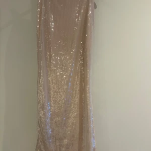 Champagnefärgad paljettkjol  - Glittrig långkjol från & Other Stories i en lyxig champagnefärg (ljusrosa). Den är täckt av paljetter, har en rak passform och slits nedtill. Perfekt för dig som vill sticka ut med en elegant och trendig look.