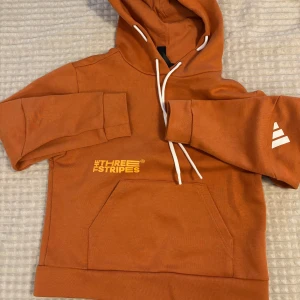 Adidas hoodie  - Cool orange hoodie från Adidas Unik detalj med knappar längs ryggen. Lite nopprig på ena sidan men annars inget fel. Inte använd på flera år. 