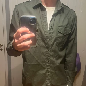 Mörkgrön skjorta/overshirt - Snygg mörkgrön skjorta eller overshirt med två bröstfickor med lock och knapp. Slim fit. Han på bilden är 184cm 70kg