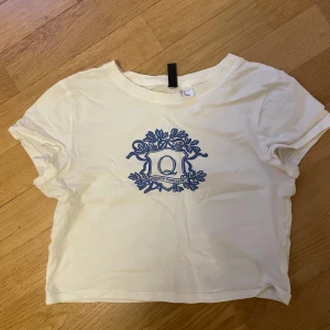 Vit topp med blått tryck från Divided- Baby tee cute y2k Coquette  - Vit Babytee från Divided med snyggt, gulligt blått tryck. T-shirten har rund halsringning och är i mjuk bomull, perfekt för en chill och stilren look. Har endast använt ett fåtal gånger och är i mycket bra skick. Tröjan är i storlek S och från Hm. Pris kan diskuteras! Rabatt vid bundle.