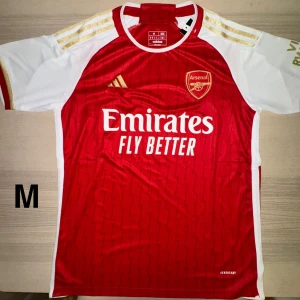 Arsenal matchtröja - Stilren och officiell Arsenal hemmatröja i storlek M – perfekt för alla Gunners-fans! Tröjan är  med “Emirates Fly Better”-tryck och klubbemblem broderat på bröstet.  🔴 Ikonisk röd design med vita och guldiga detaljer ✅ Storlek: M (medium) 👕 AEROREADY-material – andas och transporterar bort fukt 🆕 Helt ny med taggar kvar  Perfekt till matchdagar, träning eller som en cool vardagströja! Säkra din Arsenal-look idag ⚽🔥