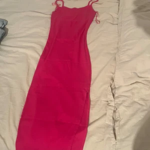 Rosa långklänning med smala axelband - Snygg rosa långklänning med smala axelband och slits på sidan. Klänningen har en figurnära passform och är perfekt för dig som vill sticka ut. Enkel och stilren design som ger en trendig look.