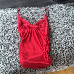 Röd spetslinne med smala axelband - Snygg rött linne med smala axelband och v-ringning. Överdelen har fina spetsdetaljer och en liten rosett framtill. Materialet känns mjukt och följsamt. Storleken är i XS/S. Kan anpassa banden. Inte använt många gånger alls.