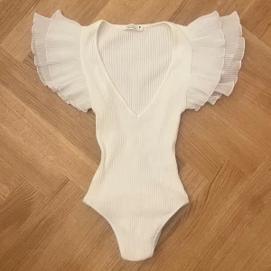 Vit volang body  - Supersnygg vit ribbad body med djup v-ringning och stora plisserade volangärmar💘Kroppsnära passform som framhäver figuren. Perfekt för Stockholmsstil 💓💓Jag tycker att storleken passar XS-S. Den är helt ny, endast testad☺️ Tryck gärna på köp nu!!