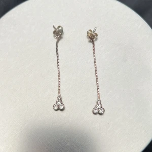Långa silverörhängen med stenar - Säljer ett par eleganta, långa örhängen i silverfärg med tunn kedja och tre gnistrande stenar längst ner. Perfekta för att ge en stilren och glittrig touch till din look.