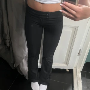 Svarta bootcut-byxor  - Säljer ett par svarta bootcut-byxor från Nelly i storlek XS. Byxorna har hög midja, två knappar framtill och är stretchiga för en bekväm passform. Innerbenslängd är 71 cm men kan justeras till normal längd. Perfekta till en snygg och enkel look💗