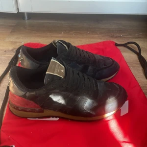 Valentino Rockrunner sneakers svart/röd - Snygga Valentino Rockrunner sneakers i svart och rött med coola stjärnmönster och nitar på hälen. Ovandel i skinn och mocka, klassisk snörning och gummisula. Perfekta för dig som vill sticka ut med exklusiva detaljer och streetkänsla. Lite slitna på ett ställe som ni ser men tvättar såklart innan jag skickar Tyvär ingen box då dem är köpt av en vän från hockey laget.