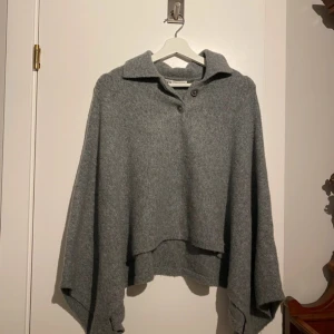 Poncho från Zara! - Grå stickad poncho från Zara! Mysig grå  poncho från Zara med krage och knapp framtill. Ponchon har långa, vida ärmar och en avslappnad passform. Perfekt för kyliga dagar och enkel att styla till olika outfits. Ny utan prislapp!  Aldrig använd! 