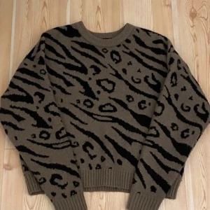 Brun och svart mönstrad tröja från Pieces! Fint skick! - Säljer en snygg brun tröja från Pieces med  svart zebramönster. Tröjan har långa ärmar och ribbade muddar vid ärmslut och nederkant. Perfekt för att ge din outfit en cool touch 🖤färgen i botten är en blandning av grön grå brun. Den är verkligen jättefin och varm! Finns lite noppror som på alla stickade tröjor, men de syns knappt! 