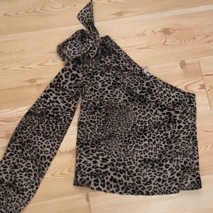  oneshoulder topp från Nelly! -  Snygg topp med leopardmönster i beige och svart. Modellen är oneshoulder med en lång ärm och en axel bar. Tunt och lätt material som ger en cool och trendig look.  dig som vill t använd 2  gånger! 