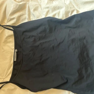 Svart linnetopp men vet inte riktigt var den är från - Enkel och stilren svart linnetopp f med tunna axelband. Perfekt att matcha med jeans eller kjol för en clean look. Mjuk och skön bomullskänsla, passar året runt.
