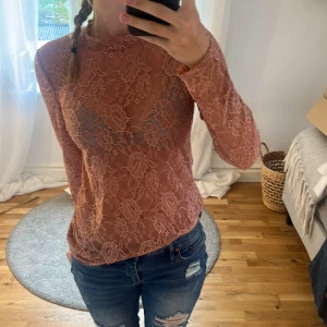 Rosa spetsblus med lång ärm - Säljer en superfin rosa blus i genombruten spets med blommigt mönster. Blusen har lång ärm och en tight passform som sitter snyggt på kroppen. Perfekt att styla med jeans eller kjol för en trendig look.