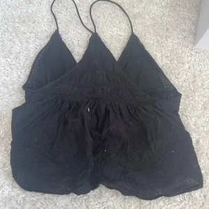 Svart broderad linnetopp från Zara - Supersöt svart linnetopp från Zara med tunna axelband och v-ringning. Toppen har broderade detaljer och lätt volang nedtill, vilket ger en bohemisk vibe. Perfekt till jeans eller kjol när du vill ha en chill men snygg look.