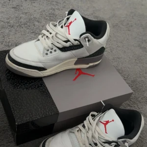 Nike Air Jordan 3 Retro White/Black - Nike Air Jordan 3 Retro i vitt och svart skinn med ikoniska elefantmönstrade detaljer. Röd Jumpman-logga på plösen och AIR-tryck bak. Klassisk siluett med snörning, rund tå och vadderad insida för extra komfort. Perfekta för dig som vill sticka ut med en tidlös sneaker