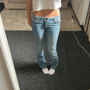 Ljusblå bootcut jeans låg midja - Säljer ett par ljusblå jeans med bootcut passform och låg midja. Klassisk femficksmodell med dragkedja och knapp framtill. Jeansen är i mjukt denimtyg och har en snygg, avslappnad vibe. Perfekta för dig som gillar retrostil och vill ha ett par jeans som sitter skönt på höften.