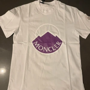 Vit Moncler t-shirt med lila logga - Helt ny moncler T-shirt köpt från Farfetch för drygt 4000kr. Har haft den hemma bara inte använt den.  Pris kan diskuteras!