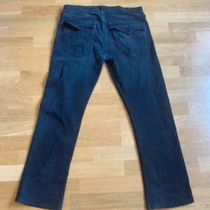 True Religion Ricky svarta jeans 34 - Svarta jeans från True Religion, modell Ricky Relaxed Straight. Klassisk femficksdesign med raka ben och snygga ficklock bak. Jeansen är tillverkade i bomull och har en avslappnad passform som ger en chill vibe.