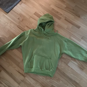 Grön hoodie med huva och magficka - Snygg grön hoodie med huva och dragsko, perfekt för chill dagar. Tröjan har en stor magficka och långa ärmar. Mjuk och skön, passar dig som gillar en avslappnad stil.