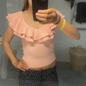 Ljusrosa volangtopp med struktur - Supersöt ljusrosa topp med dubbla volanger över axlarna och en smickrande, croppad passform. Toppen har en strukturerad, lätt skrynklig yta och är ärmlös. Perfekt för dig som gillar romantiska detaljer och vill sticka ut lite extra.