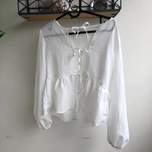 Vit blus med knyt - Superfin vit blus med långa ärmar, knyt framtill och volang nedtill. Blusen har lätt tyge och en luftig känsla. Jag kan ej knyta över brösten (har 75B) passar nog bättre på A. Även jättefin att ha den bak o fram att där man knyter är på ryggen, jätte fint.