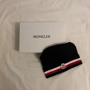 Moncler mössa - Svart moncler mössa väldigt snygg, oanvänd med prislapp. Kommer med låda och allt annat med på bilderna, skön och har tjockt material!