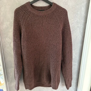 Brun stickad tröja med rund hals - Mysig brun stickad tröja med grov ribbstickning och rund halsringning. Perfekt för kyliga dagar och enkel att matcha med jeans eller kjol. Långärmad modell med avslappnad passform och klassisk look.