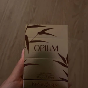 Opium parfym från Yves Saint Laurent - Opium Eau de Parfum från Yves Saint Laurent, 30 ml. Flaskan är mörkröd med gulddetaljer och rundad form, och har en lyxig guldig kork. Förpackningen är guldig med bruna bambuliknande mönster. En ikonisk och elegant doft.