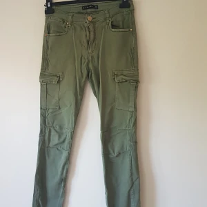 Gröna cargopants från Amisu, stl 38 - Snygga gröna cargopants från Amisu i storlek 38. Byxorna har flera praktiska fickor på sidorna och en slim passform. Perfekta för en avslappnad streetstil och tillverkade i mjuk bomullskänsla. Klassisk cargodesign med knapp och dragkedja framtill.  Helt & fint skick