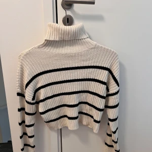 Randig polotröja från NA-KD Reborn XS - Superfin ribbstickad polotröja från NA-KD Reborn i vitt med svarta ränder. Croppad modell med lång ärm och hög polokrage.