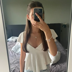 Vit topp från Gina Tricot - Supersöt vit topp från Gina Tricot med v-ringning och korta, vida ärmar. Perfekt att styla med jeans eller kjol för en fräsch look.
