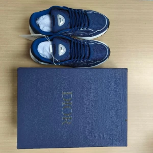 Blå Dior b30 - Snygga blå sneakers från Dior med vit och svart sula. Skorna har silverfärgade detaljer och tydlig Dior-logga på sidan. Ovandelen är i mesh och syntet för en sportig look. Perfekta för dig som vill sticka ut med exklusiva sneakers.