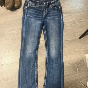 Miss Me jeans med broderade fickor - Snygga blå jeans från Miss Me med kontrastsömmar och broderade bakfickor med paljettdetaljer. Jeansen har en klassisk femficksmodell, låg midja och bootcut ben. Perfekta för dig som gillar statement-detaljer och cool stil. 
