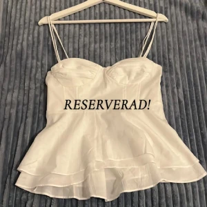RESERVERAD! Vit volangig korsettopp 🤍 - Supersöt vit korsettopp från Zara med tunna axelband och volangig nederdel, storlek S. 💓Toppen har markerade kupor och smock i ryggen för extra komfort. 😍Helt ny, använt den en gång när jag provade den. Säljer endast för att den var för liten för mig. Hann riva av lappen innan jag provade toppen, så den sitter inte kvar. 🥰