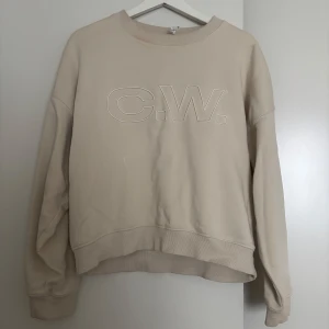 Beige/vit sweatshirt från Carin Wester - Beige/vit sweatshirt från Carin Wester med broderad logga framtill. Tröjan har rund halsringning, ribbade muddar och en relaxed passform. Perfekt för en chill och stilren look. Tillverkad i mjuk bomull som känns skön mot huden.