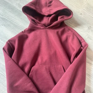 Vinröd hoodie med huva - Enkel och snygg vinröd hoodie med huva och magficka. Tröjan har ribbade muddar vid ärmslut och nederkant, samt en klassisk passform. Perfekt för dig som gillar en chill och avslappnad stil.