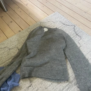 Grå stickad tröja  - En enkel och stilren grå stickad tröja med rund halsringning och långa ärmar. Tröjan har ribbade muddar vid ärmslut och nederkant, perfekt för lager-på-lager under kyliga dagar.