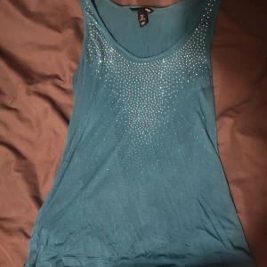 Glittrig topp - Snygg turkos linnetopp från H&M i mjuk bomull. Toppen är ärmlös och dekorerad med glittrande strass framtill som ger en cool effekt. Köpt på vinted 