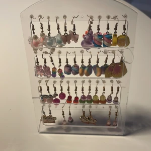 Färgglada örhängen i olika former - Säljer ett set med 20+ par örhängen i olika färger och former. Här finns allt från pastellfärgade fjärilar, pärlor, regnbågsfärgade bollar, lila ankor, godisliknande snurror till citronskivor och glittriga kulor. Perfekt för dig som gillar att mixa och matcha din stil!