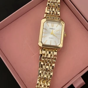 Guldig fyrkantig klocka  - Stilren klocka  med fyrkantig urtavla i vitt och detaljer i guld. Armbandet är länkformat och helguldigt, vilket ger en lyxig känsla. Perfekt accessoar för att lyfta din outfit med en elegant touch. Klockan ör helt ny och oanvänd